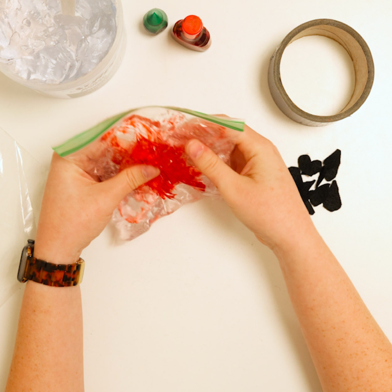 Use both hands to squish and mix a pink fruit sensory bag on a table, moving the gel and foam seeds around